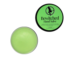 2 oz black tin of Bewitched Hand Salve with green label pictured with the lid off to show the green hand salve inside 